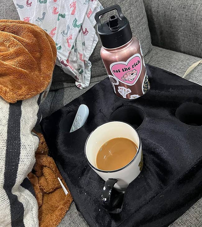 reviewer photo of the black square pillow holding a coffee mug, remote, and large water bottle