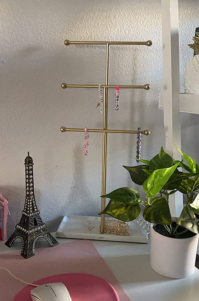 A reviewer's three tiered gold stand with bracelets hanging on it