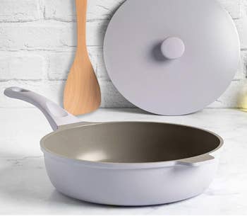Non-stick frying pan with a pale purple finish, next to a wooden spatula and white lid