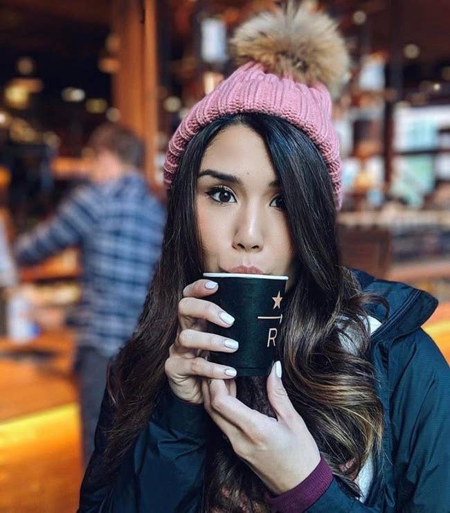 reviewer sipping a drink wearing the beanie in pink