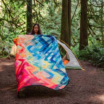 model unfurling rainbow puffy blanket at campground