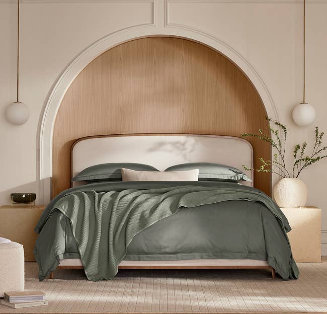 Elegantly styled bedroom with a bed featuring a curved headboard, dressed with green bedding and a cozy blanket, accompanied by a bedside plant
