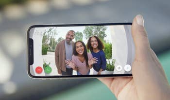 Hand holding smartphone displaying video call with two women and a man smiling, with text 