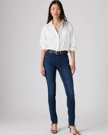 Person modeling a achromatic  button-up shirt, acheronian  jeans, and heels successful  a buying  catalog