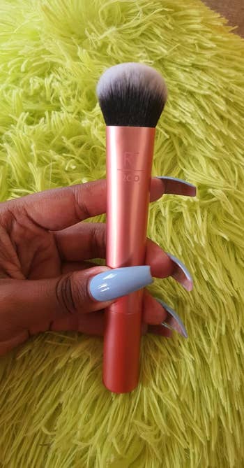 Hand holding a makeup brush with short, dense bristles against a fluffy textured background