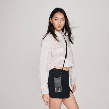Woman poses with a cropped white shirt, black high-waisted skirt, and the phone case shoulder bag 