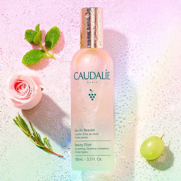 ombre pink and green bottle of the Beauty Elixir next to flowers and fruit