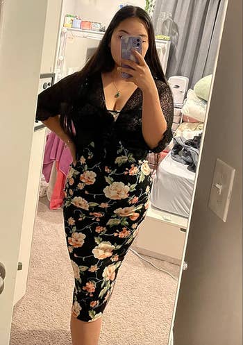 Person in a black floral dress taking a mirror selfie in a bedroom
