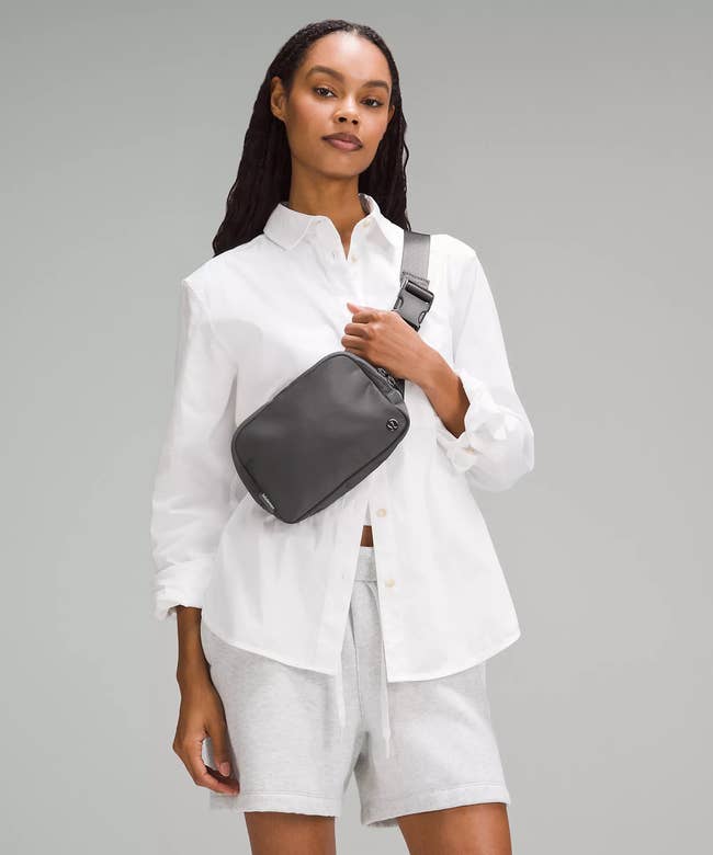 Model wears a white shirt, gray shorts, and a gray shoulder bag