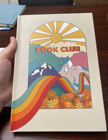 Reviewer holding a book reading journal with a color rainbow nature scene design on the cover 