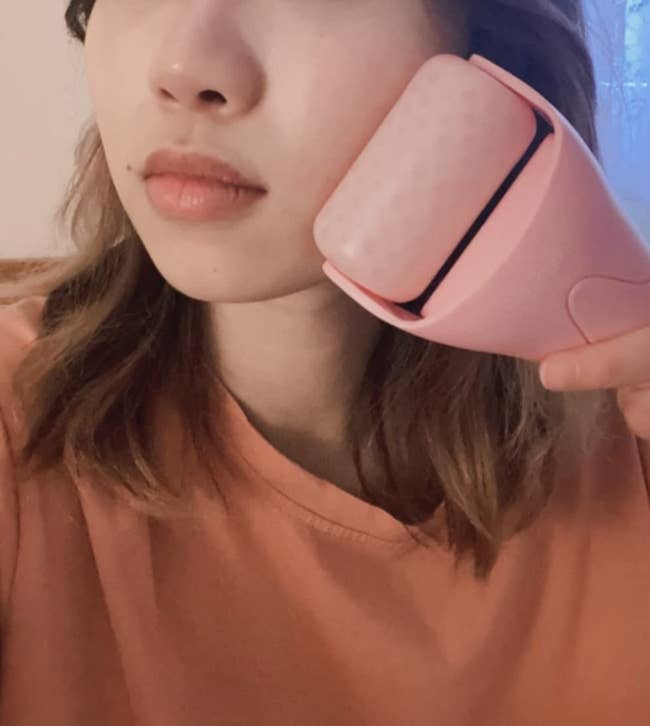 Person utilizing a facial roller connected  their cheek, demonstrating a skincare tool