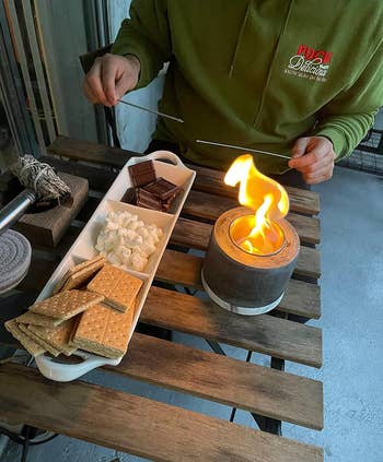 A reviewer photo of a plate with crackers, marshmallows, and chocolate next to the fire pit to make s'mores
