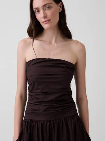 Person wearing a strapless, ruched formal with a flowing skirt, lasting against a plain background