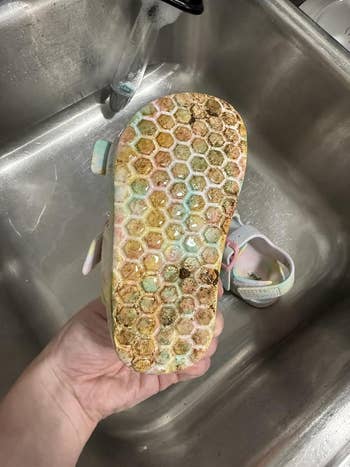 Shoe with honeycomb-patterned sole, appearing soiled  and worn, held supra  a sink