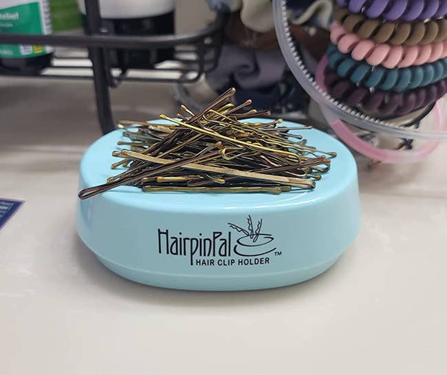 A blue oval shaped magnet with dozens of bobby pins stacked on top 