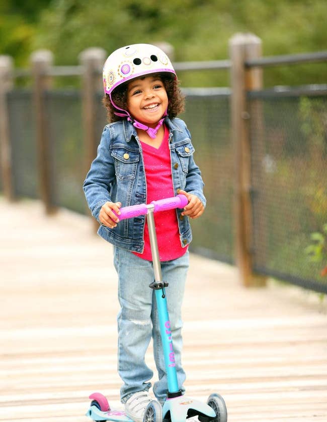 Child model with helmet riding turquoise scooter