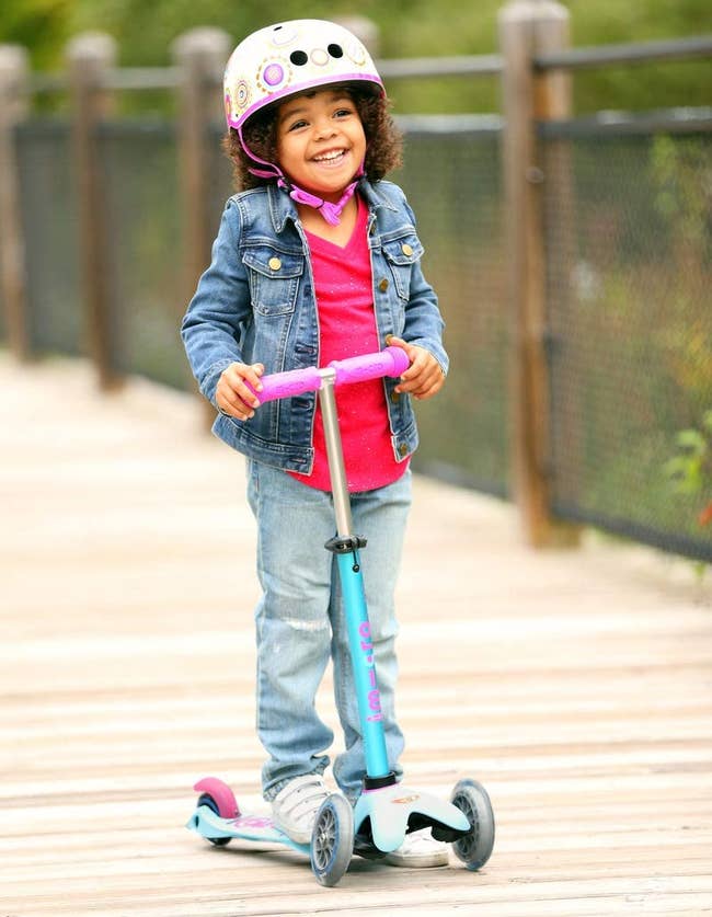 Child model with helmet riding turquoise scooter