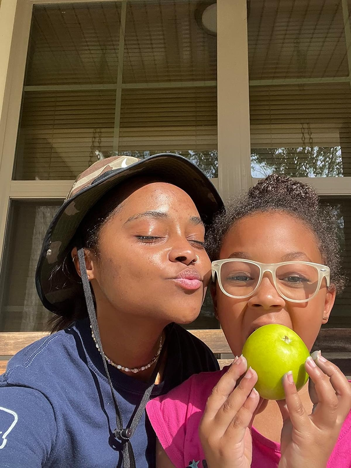 Two radical   sitting connected  a porch; 1  wears a hat, the different   holds an pome  and wears glasses