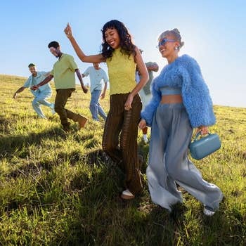 Group of six radical joyfully walking successful a field, wearing stylish, casual outfits. Two women successful the beforehand are smiling and interacting