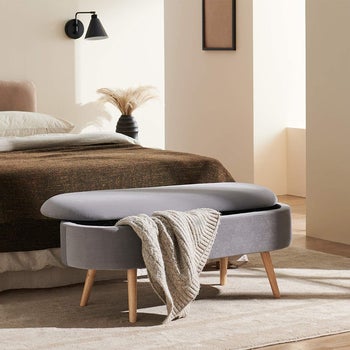 the storage bench in front of a bed with a blanket hanging from it