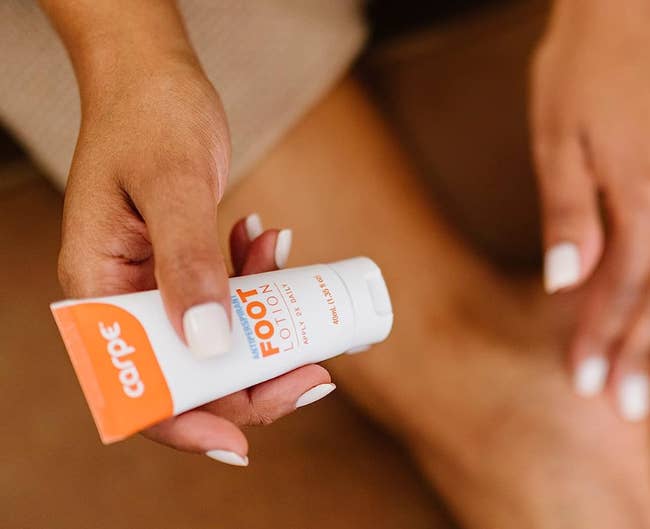 Person applying foot cream from an orange and white tube