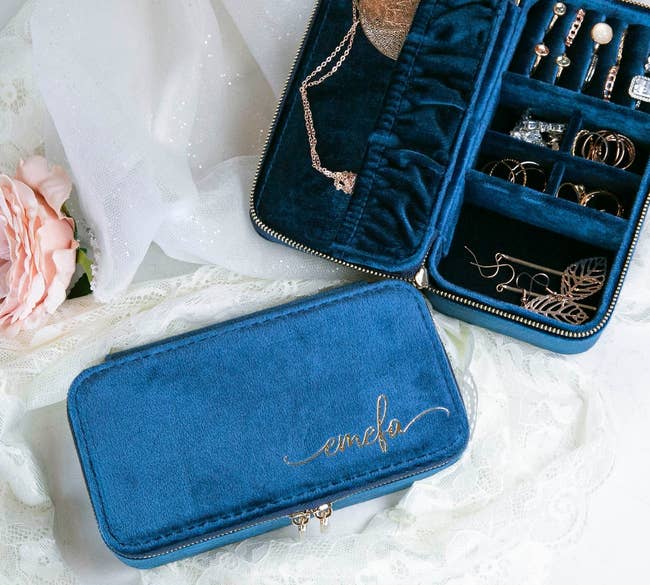 blue jewelry case open showing necklace hooks and ring rolls with a closed case beside it, both on a lace background