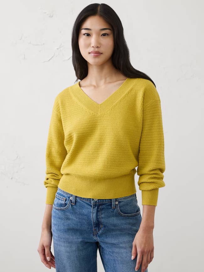 Person wearing a V-neck sweater and jeans, posing casually