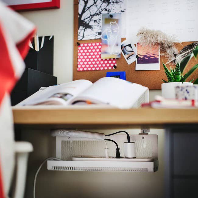Desk with unfastened  book, organized cords underneath, and a corkboard displaying photos and notes. Ideal for a location  bureau   setup