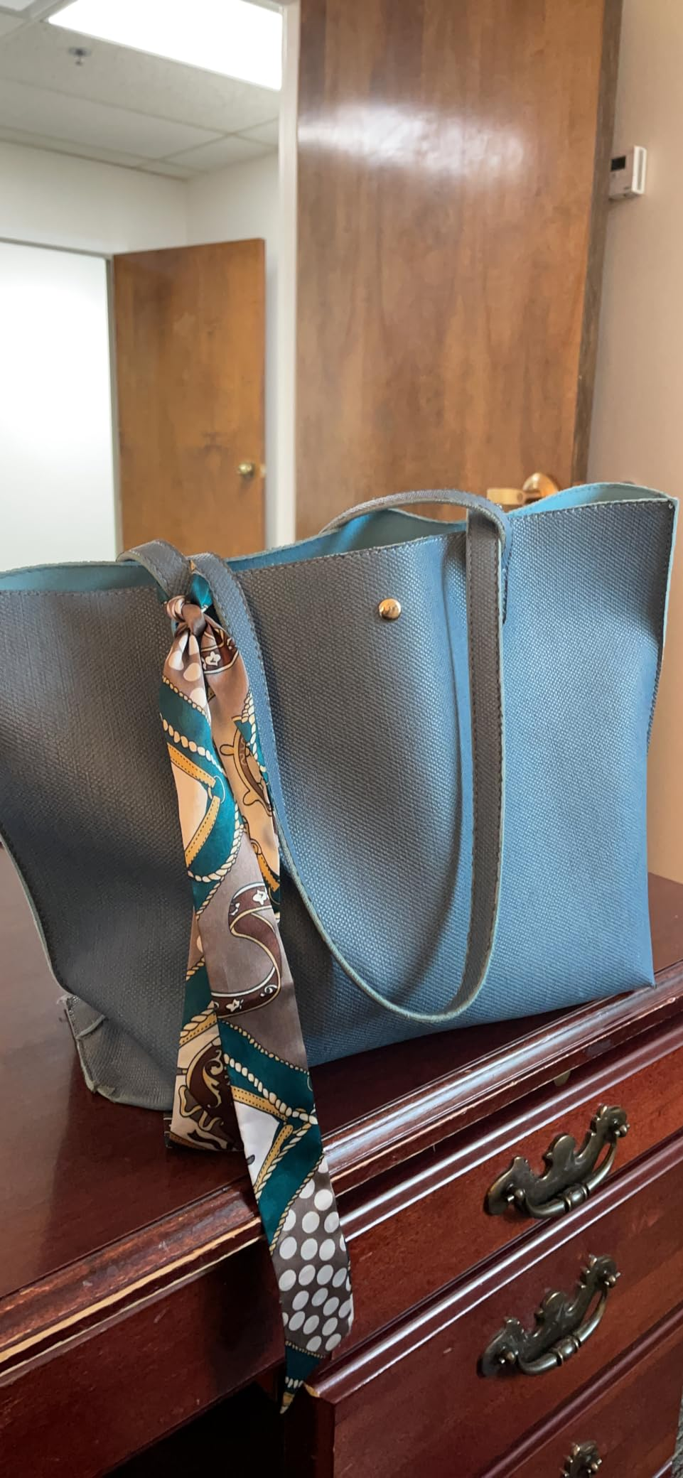 Elegant tote container  connected  a woody  dresser, accented with a patterned scarf
