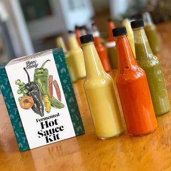 Hot sauce kit with three bottles of sauce on a wooden table, promoting DIY sauce-making for flavorful dishes
