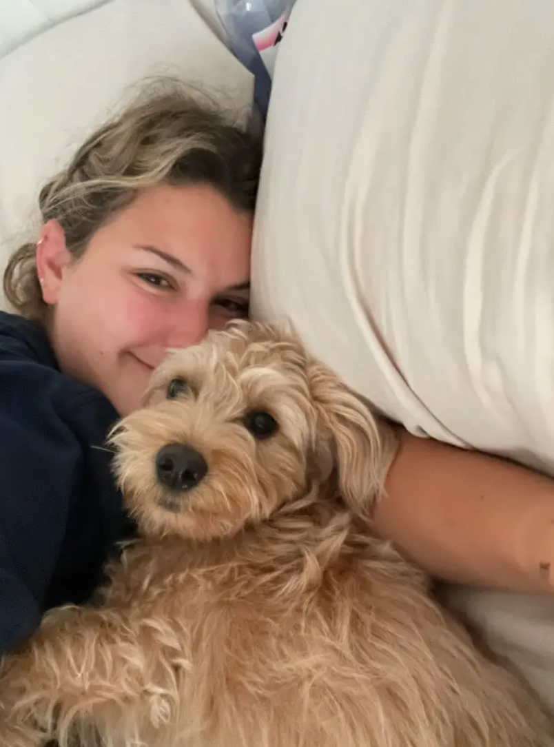 pic of Ali laying down on the white sheet set with her dog