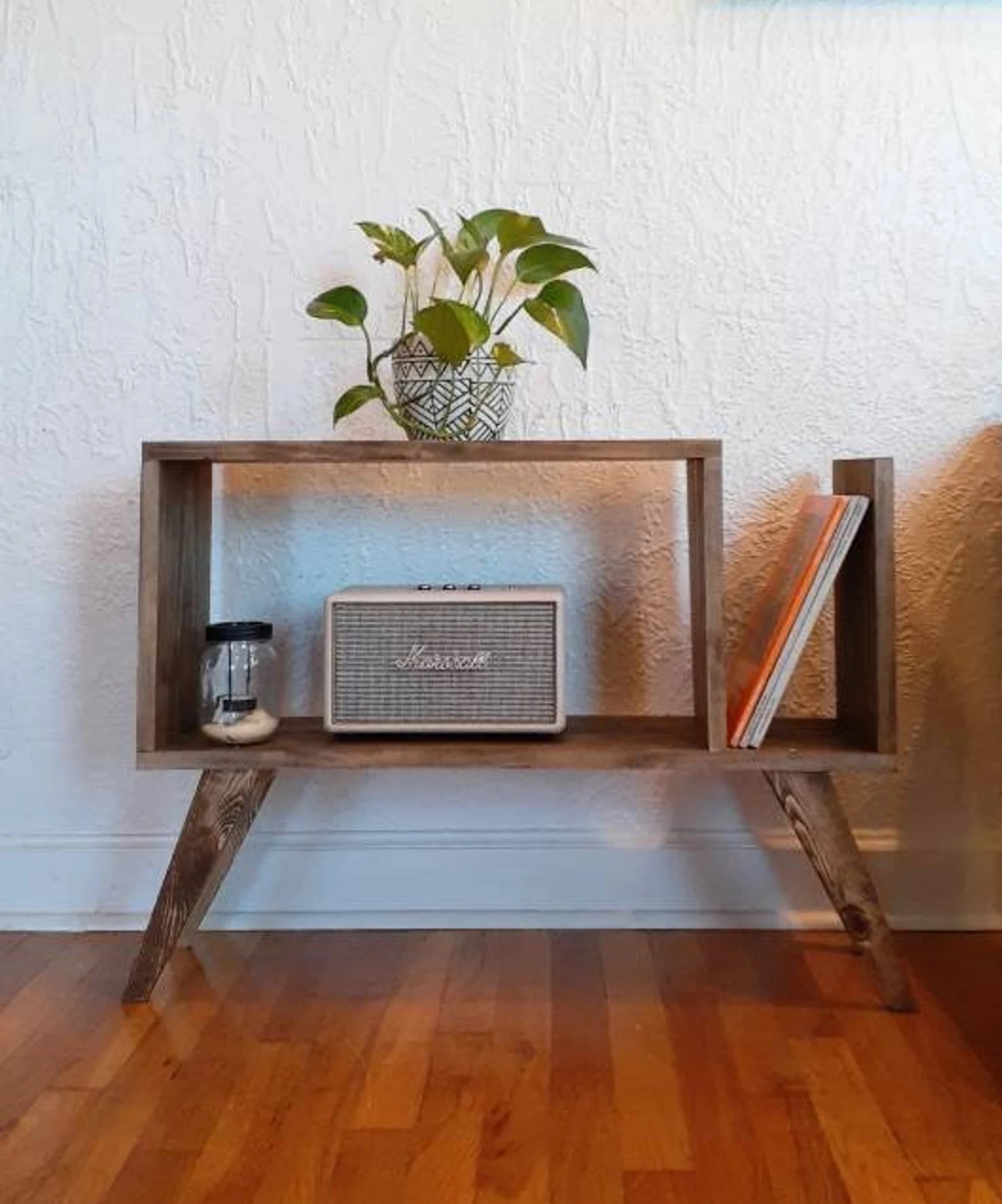 the wooden table holding a vintage radio, jar, plant, and records
