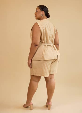 Person wearing a stylish sleeveless beige top with matching shorts and block heels, posing against a neutral background