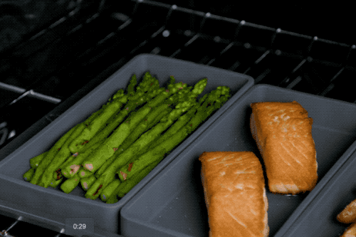 a model pulling asparagus from the oven and putting salmon and potatoes back in
