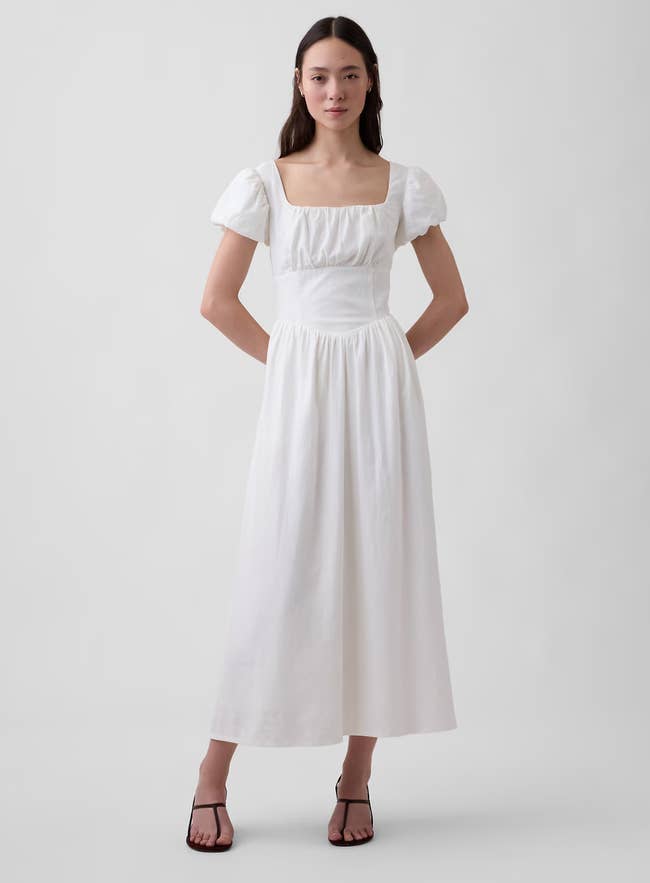 Person wearing an elegant, flowy formal  with puffed sleeves and a quadrate  neckline, styled with minimalist strappy sandals