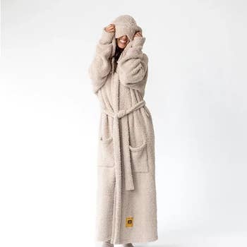 Person successful a fluffy, belted bathrobe playfully covering their face, with heavy pockets and a cozy, relaxed fit