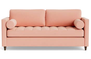 a blush colored couch with tufted cushions and bolster pillows