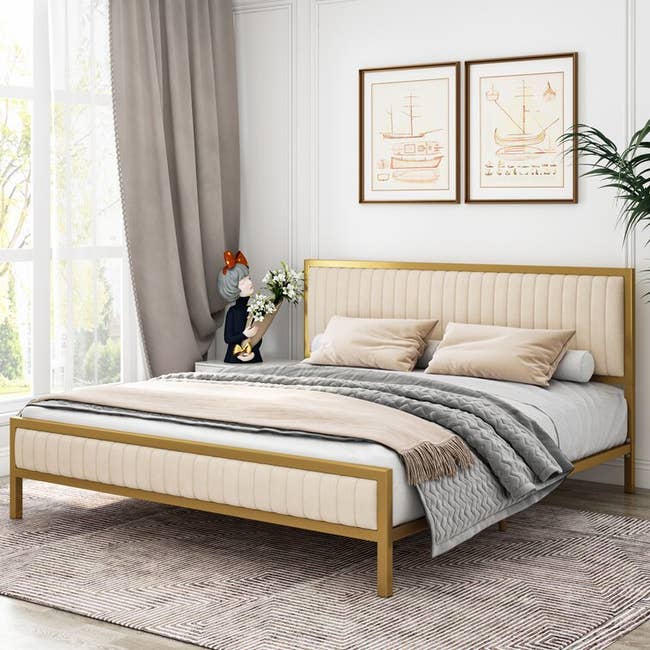 a bed frame with cream-colored tufted upholstery and gold framing