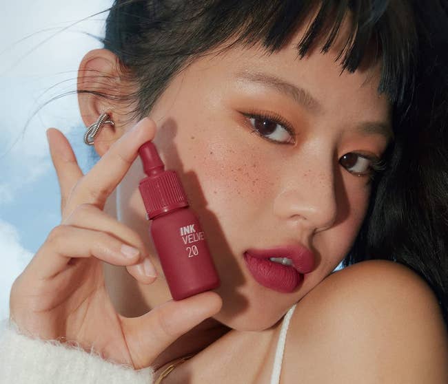model wearing shade 'classy plum rose' and holding up lip tint bottles