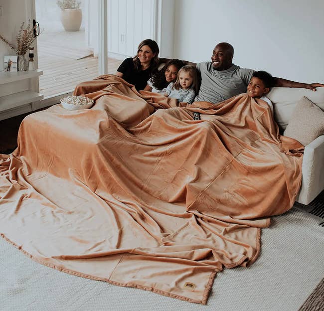 family laying underneath huge throw blanket on couch in the color camel