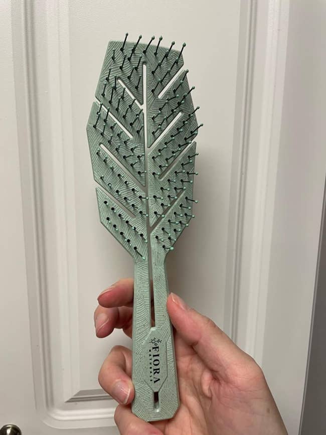 A reviewer holding a leaf-shaped hairbrush