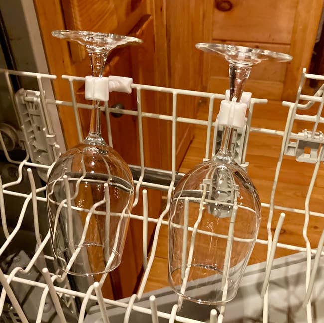 Two wine glasses secured upside down in a dishwasher rack by the white clips