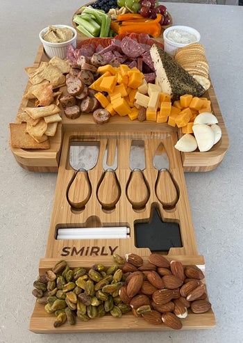 reviewer photo of the charcuterie board filled with meats, cheese, crackers, vegetables, and nuts, with the drawer slid out to show the four serving utensils and other accessories