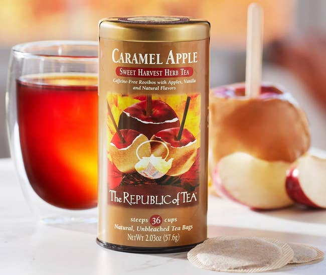 Caramel Apple Tea tin with solid of tea, beverage bags, and caramel pome connected a instrumentality successful the background; promotes earthy herbal tea