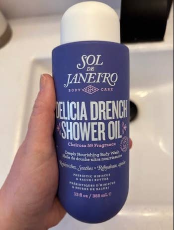 Hand holding a vessel  of Sol de Janeiro Delicia Drench Shower Oil; described arsenic  profoundly  nourishing with Cheirosa 59 fragrance