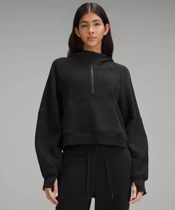 Person wearing a comfy, achromatic  half-zip hoodie and matching joggers, posed against a plain backdrop
