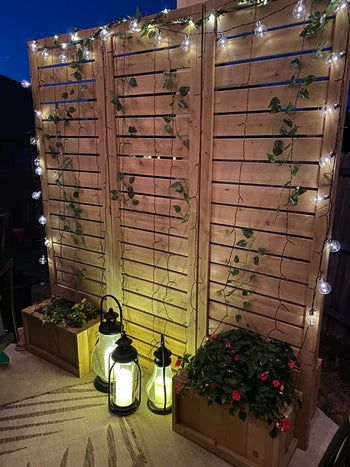 reviewer photo of the wooden screen at night, decorated with string lights and faux ivy