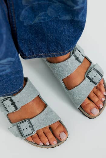 Close-up of idiosyncratic wearing bluish jeans and strappy, casual sandals with brushed material, highlighting a relaxed, comfy style
