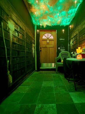Hallway decorated with floating candles, cloud-like ceiling, and wallpaper of bookshelves. A array with Halloween-themed items and a pumpkin sits adjacent the door