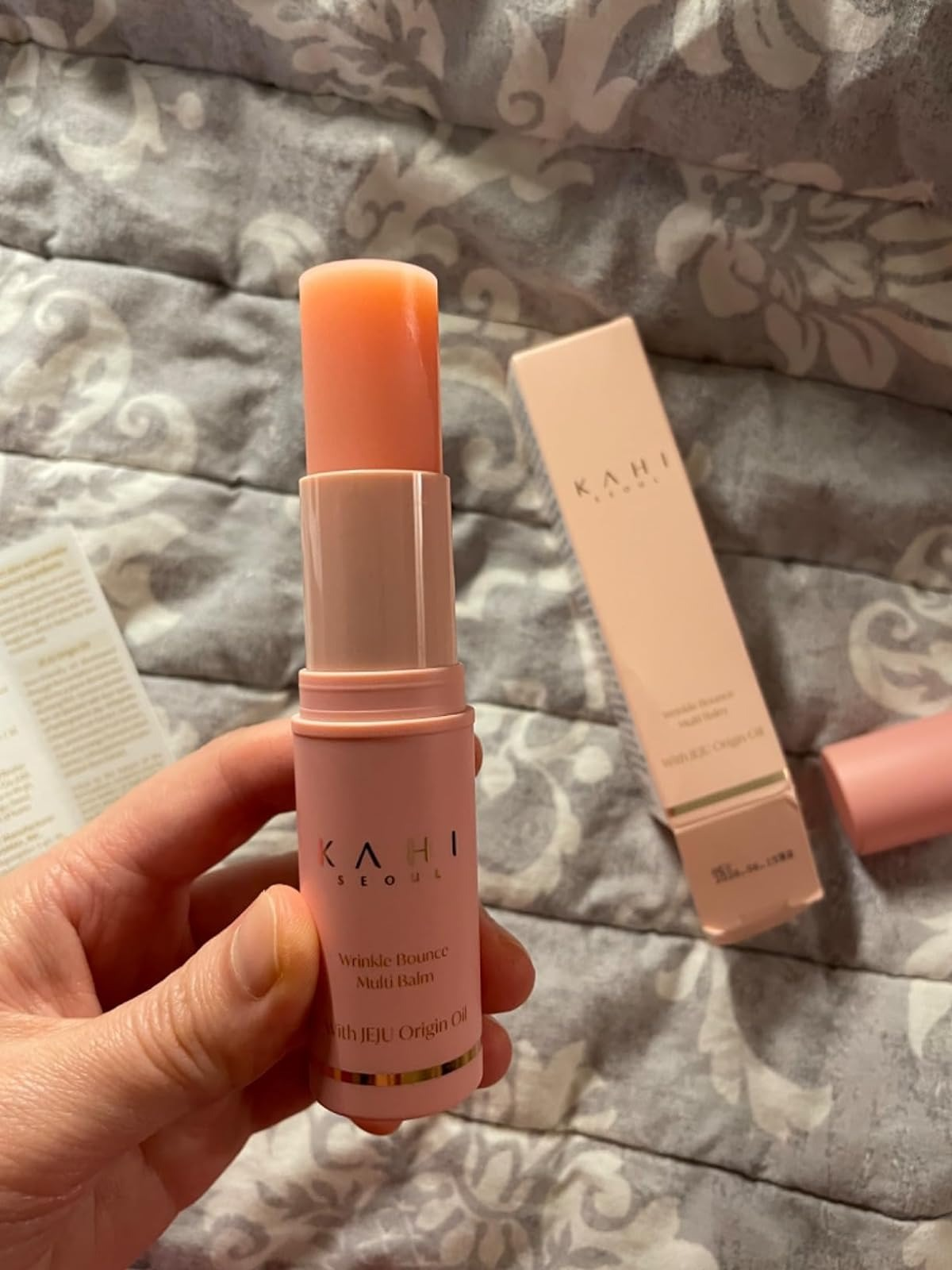Hand holding a Kahi Wrinkle Bounce Multi Balm against a background with its packaging